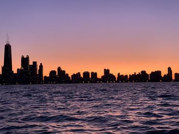 Silhouette buildings in city against clear sky during sunset