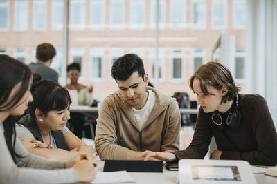 Multiracial students discussing with teacher over tablet pc in university