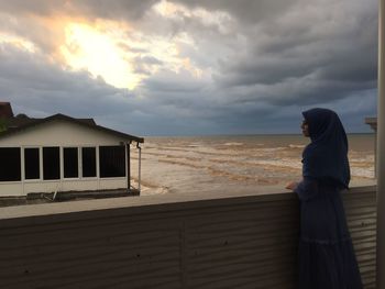 Side view of woman standing by sea against sky