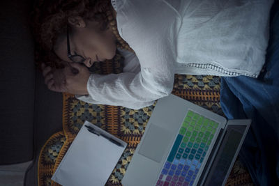 High angle view of woman sleeping by laptop and book with pen on bed at home