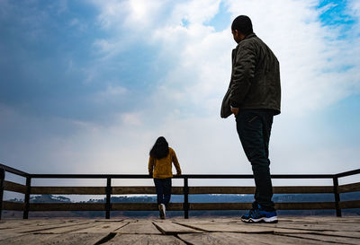 Rear view of friends standing on railing against sky