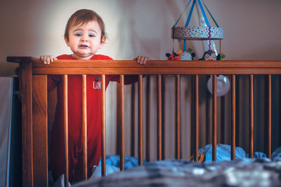 Portrait of cute baby boy standing in crib at home