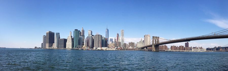 Panoramic view of brooklyn bridge over east river by cityscape against sky