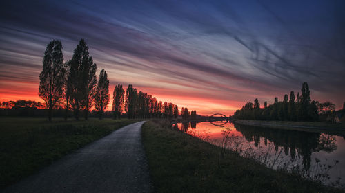 Road by trees against sky during sunset