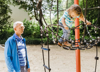 Grandfather by daughter playing in playground against trees