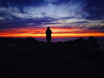 Silhouette woman standing on landscape against sky during sunset