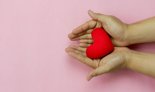 Close-up of hand holding pink flower over colored background