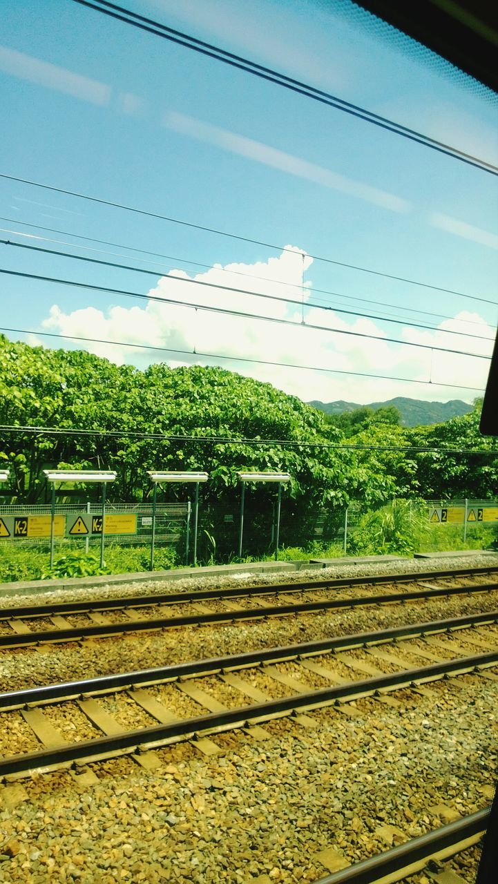 railroad track, rail transportation, transportation, public transportation, power line, growth, train - vehicle, sky, railway track, tree, field, railroad station platform, mode of transport, plant, day, railroad station, nature, green color, no people, landscape