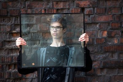 Young man holding glass against wall