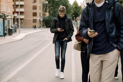 Teenage boy using smart phone while walking on street in city