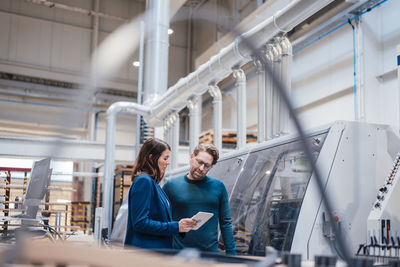 Engineer sharing tablet computer with colleague by machinery in industry