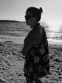 Portrait of young woman standing at beach against sky