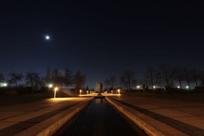 Empty road along illuminated street lights in city at night