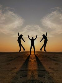 Silhouette people jumping on road against sky during sunset