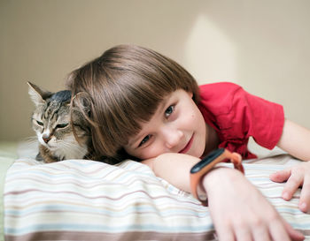 Portrait of boy with cat relaxing on bed at home