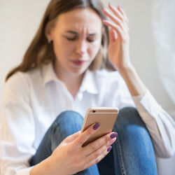 Close-up of sad woman using smart phone at home