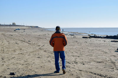 Rear view of man standing at beach against clear sky