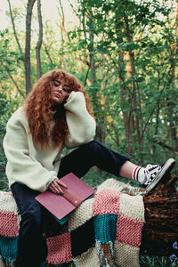 Young woman sitting on book against tree