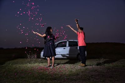 Full length of young couple standing on grass field against sky at night
