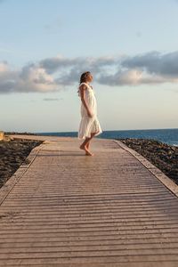 Side view of girl standing on boardwalk against sea