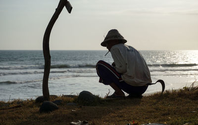 Rear view of man sitting on shore at beach against sky