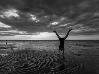 Child with handstand on beach against sky during sunset