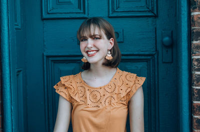 Portrait of smiling young woman sitting against door