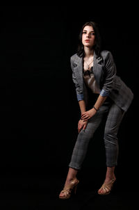 Portrait of young woman standing against black background