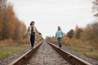 Full length of mother and son standing on railroad track against sky