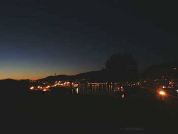 Illuminated silhouette trees by sea against clear sky at night