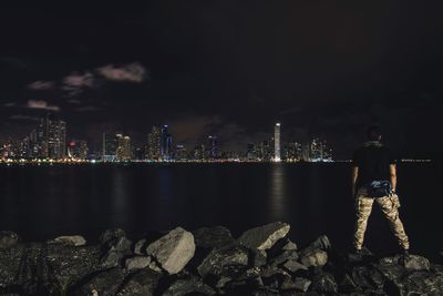 Rear view of man standing by river at night