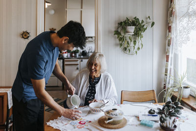 Side view of male caregiver serving water to senior woman at home