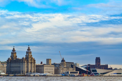 Buildings at waterfront against cloudy sky