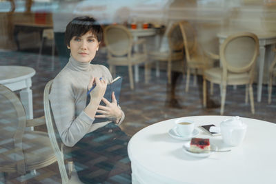 Portrait of man holding coffee while sitting on table
