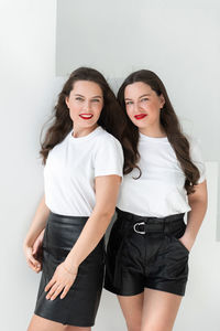 Two beautiful women twin sisters posing white background