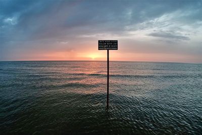 Information sign by sea against sky during sunset