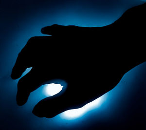 Close-up of silhouette hand against illuminated blue sky