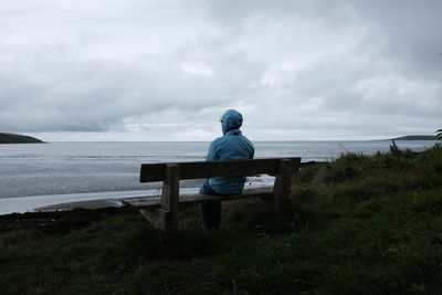 Rear view of woman sitting on bench by sea against sky