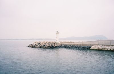 Lighthouse by sea against clear sky