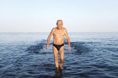 Full length of shirtless man standing in sea against clear sky