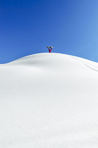 Man holding snowboard standing with arms raised at snowcapped mountain