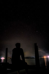 Silhouette man sitting against illuminated sky at night