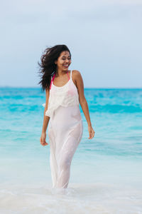 Happy young woman standing at beach against sky