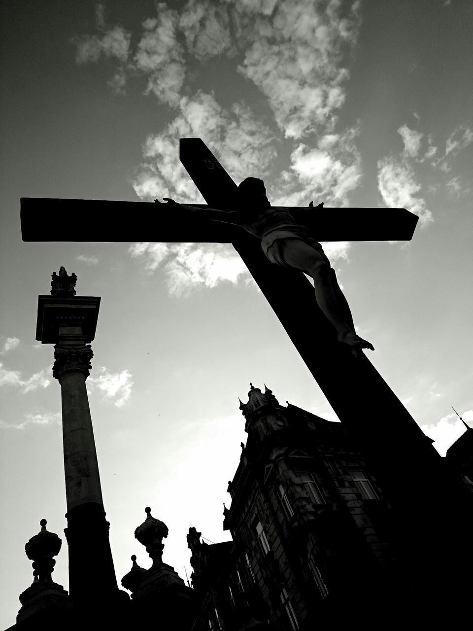 low angle view, religion, sky, cross, spirituality, place of worship, cloud - sky, human representation, church, sculpture, silhouette, statue, built structure, architecture, history, art and craft, art