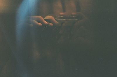 Cropped image of hands holding camera in darkroom