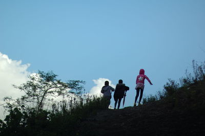 Low angle view of children climbing mountain against blue sky