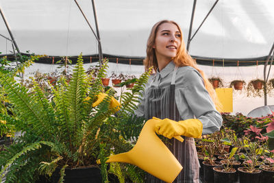 Young woman looking away while standing in greenhouse