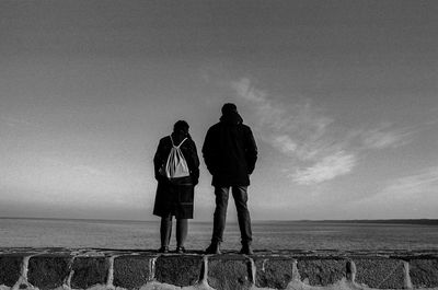 Rear view of friends standing by sea against sky