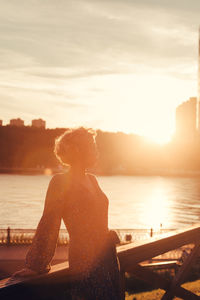 Woman standing by lake during sunset