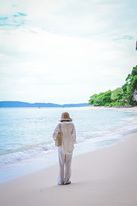 Rear view of woman standing at beach against sky